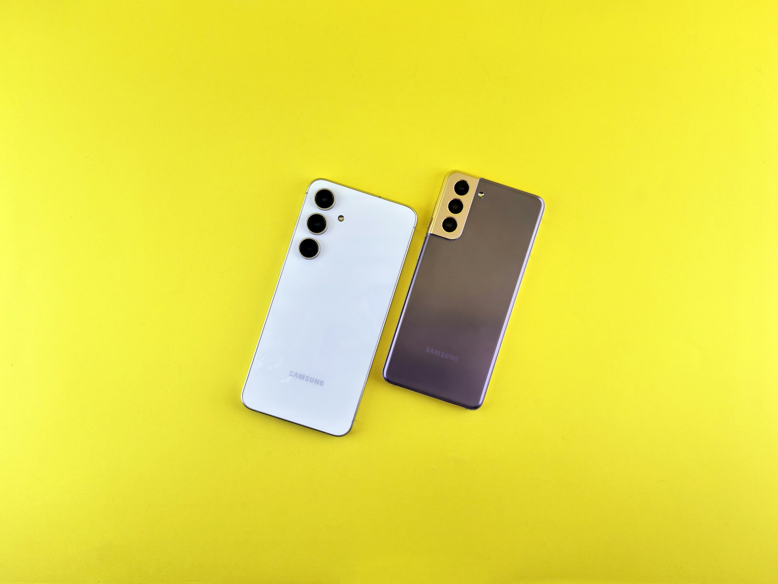 Two cell phones sitting next to each other on a yellow surface